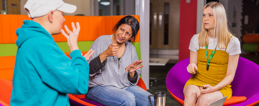 Three people sitting in a communal area and conversing.
