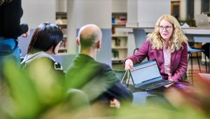 A female student pointing at laptop and talking to another female and male student