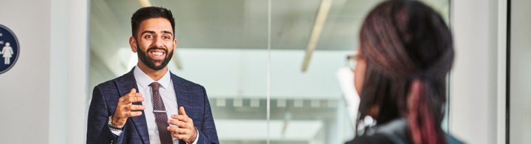 A male student smiles while talking to another student, he is wearing a suit