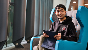 Student sat on comfy sofa chair looking at iPad