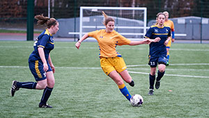 Female students playing football at Walsall Campus, on an outdoors pitch and wearing uniforms
